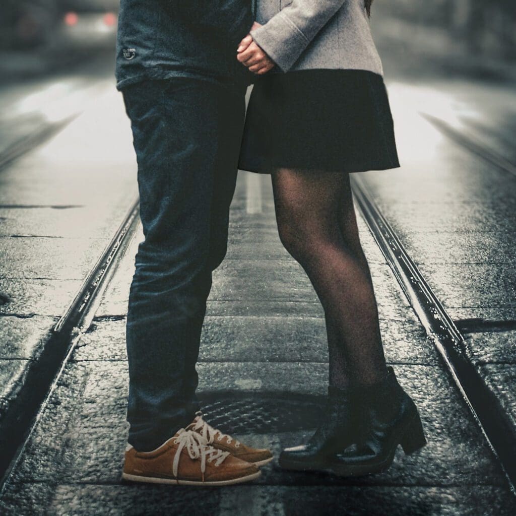 A couple kissing on a street at night.